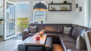 Ein modernes Wohnzimmer mit Ledersofa, Couchtisch aus Holz und einem großen Fenster mit Blick auf eine grüne Landschaft.
