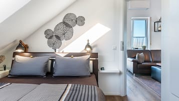 Quarto moderno com teto inclinado, uma cama grande com roupa de cama listrada, duas luminárias de cabeceira e uma obra de arte na parede.