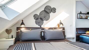 A bedroom with a skylight, a bed with striped bedding, a wall art piece, and a bedside table with lamps.