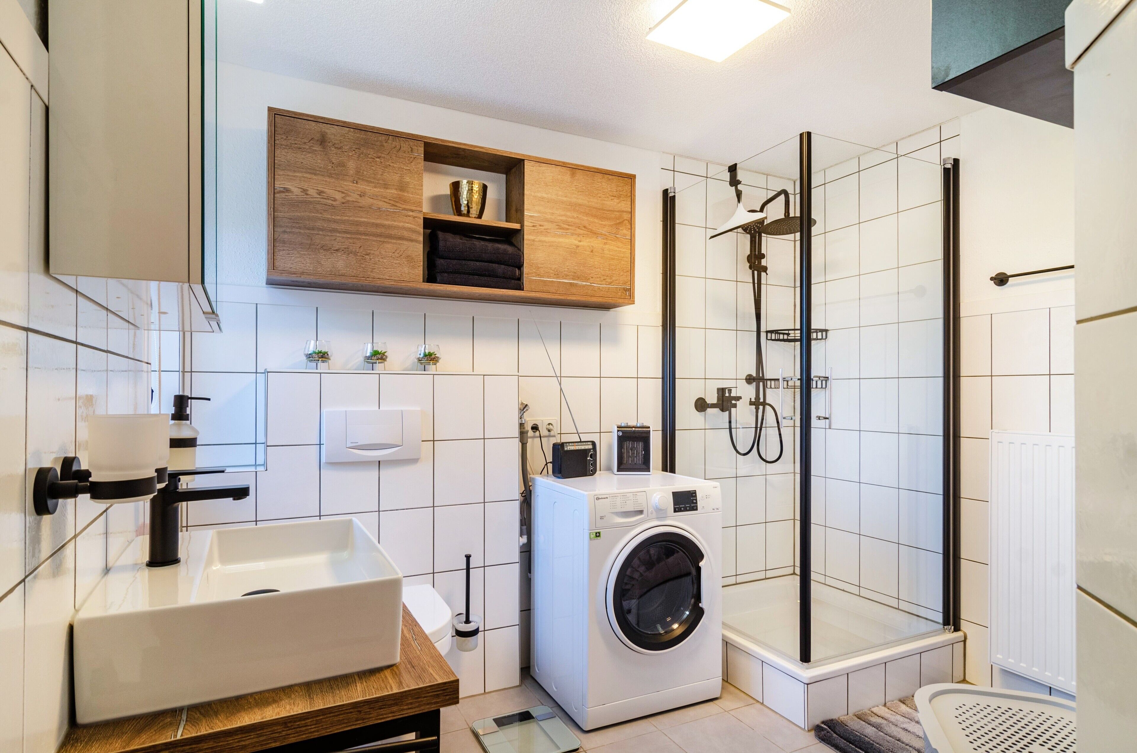 Un baño moderno con lavamanos, lavadora y cabina de ducha de vidrio.