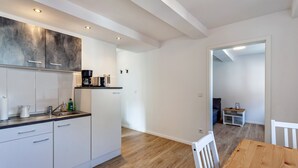 Une cuisine moderne avec des meubles blancs, une table à manger en bois et une vue sur l’espace de vie.