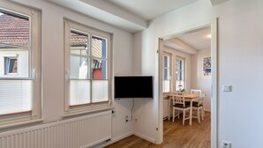 Une pièce avec un téléviseur fixé au mur, une table à manger avec des chaises et un radiateur.