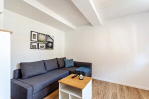 Una sala de estar moderna con un sofá gris, una mesa de centro de madera y una pared blanca con cuadros enmarcados.