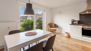 Una cocina moderna con una mesa de comedor, sillas, una lámpara colgante, una silla de mimbre, una estufa y vistas a través de un ventanal.