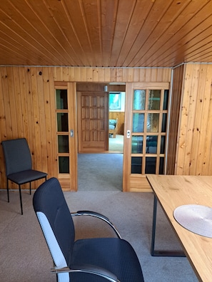 Ein Zimmer mit Holzboden, einem Tisch, zwei Stühlen und einer Tür zu einem weiteren Raum.
