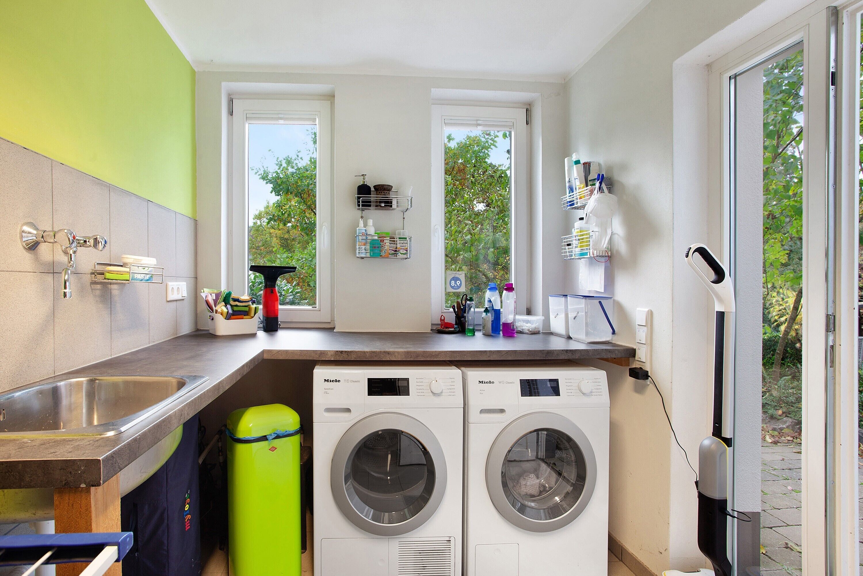 A compact laundry area with two front-loading washing machines, a sink, and a window providing natural light.