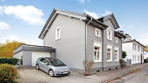 Un edificio residencial de dos plantas con fachada gris, un garaje y un automóvil estacionado.