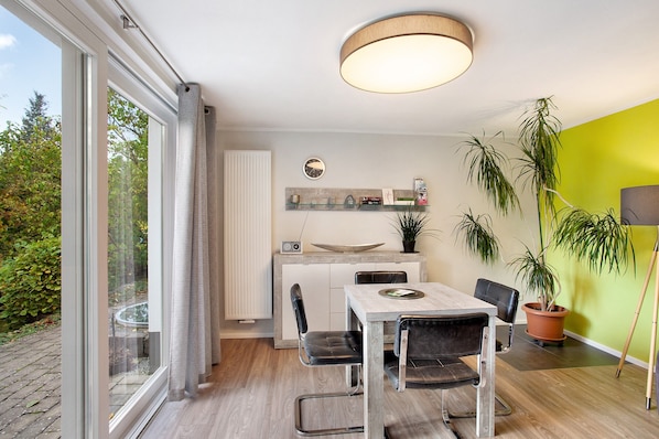 Une cuisine moderne avec un coin repas, de grandes fenêtres et des plantes en pot.