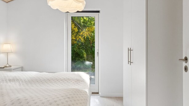 A bedroom with a bed, a bedside table with a lamp, a wardrobe, and a sliding glass door leading to a garden.