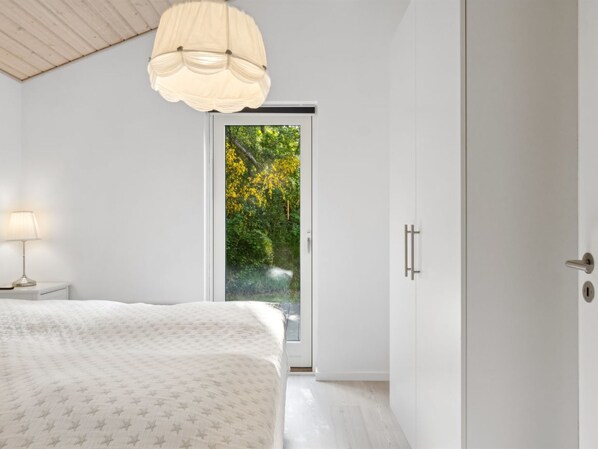 Une chambre à coucher comprenant un lit, une table de chevet avec une lampe, une armoire et une porte-fenêtre coulissante donnant sur un jardin.
