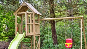 A wooden play structure with a slide and swings in a grassy area.