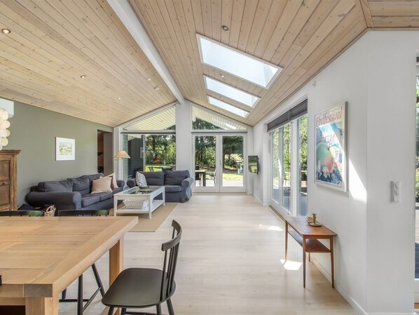 A spacious living area with a high ceiling, large windows, and a view of the outdoors.
