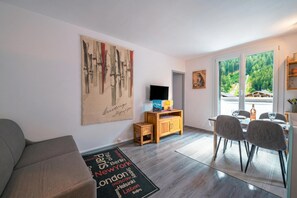 Una sala de estar moderna con un sofá, un televisor, un mueble de madera y una zona de comedor con sillas.