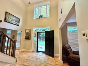 A spacious interior with a wooden floor, a black door leading outside, a brown leather chair, and a framed picture on the wall. - Woodland Retreat w/ Game Room, Fire Pit & King Suite (Greens Fork)