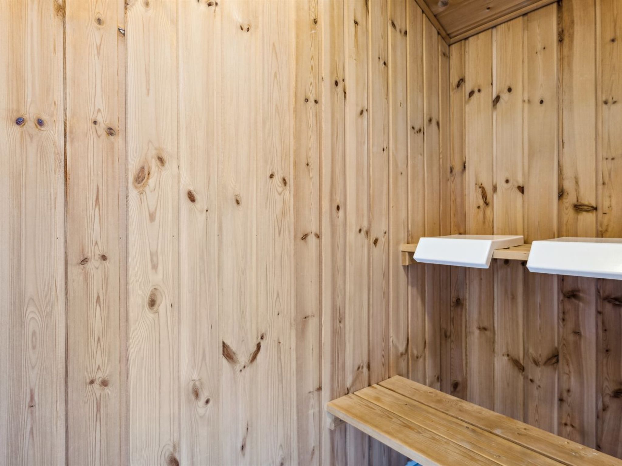 Een houten sauna met banken en een wit schap.