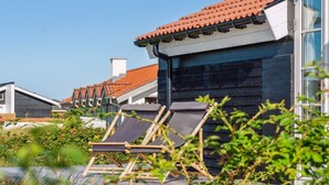 A modern building with a dark facade and a red-tiled roof. In the foreground, there are two wooden lounge chairs with dark cushions. - "Blaguna" - 600m from the sea by Interhome (Thisted)