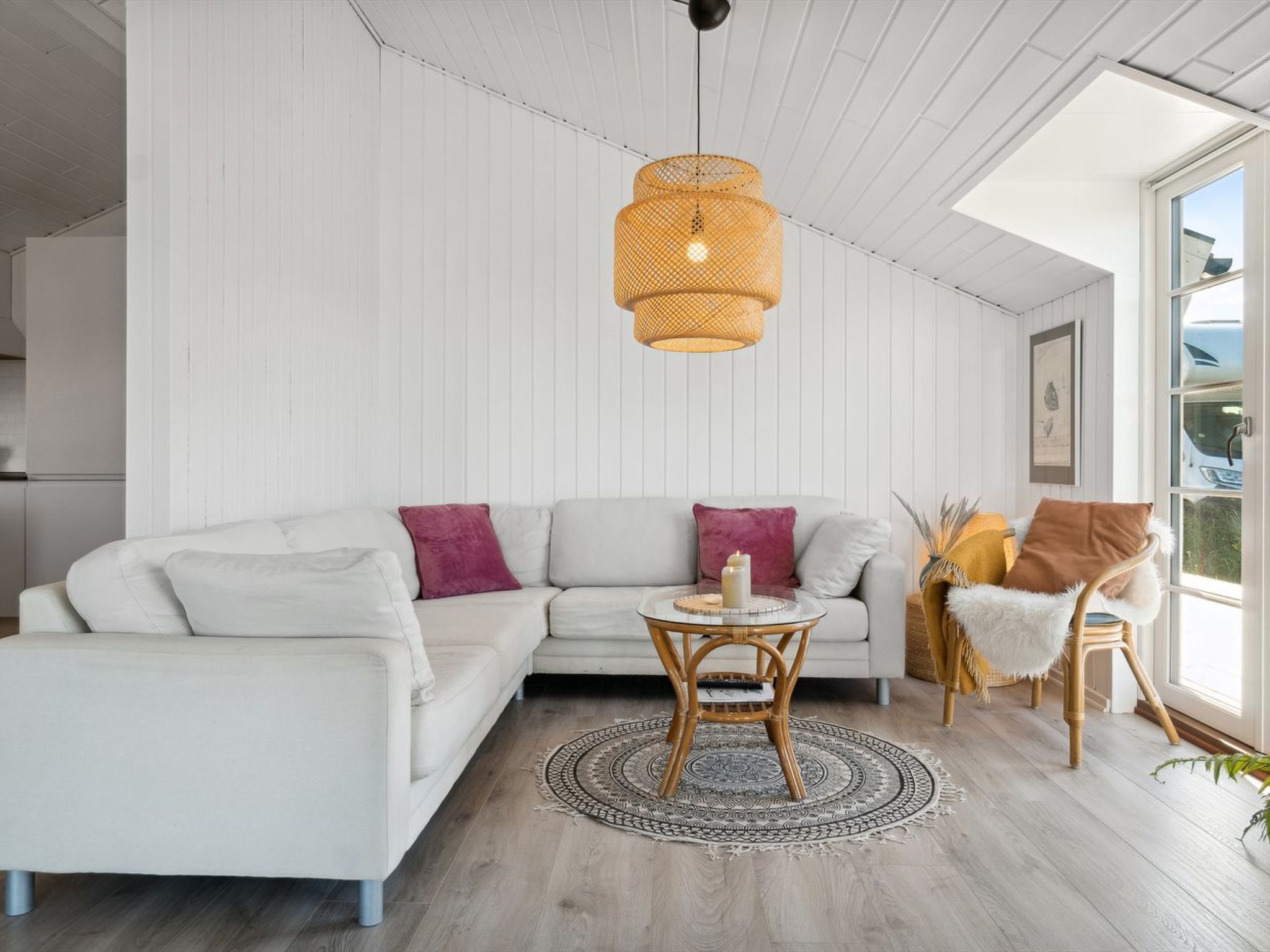 Un salon moderne avec un canapé d’angle blanc, une table basse ronde et un fauteuil en osier.