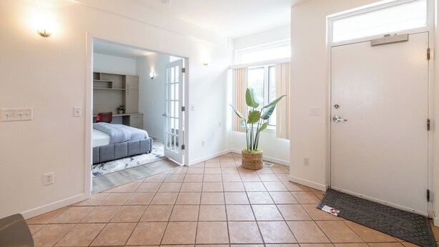 Una habitación amplia con una cama, una planta en maceta y una puerta que da a otra estancia.