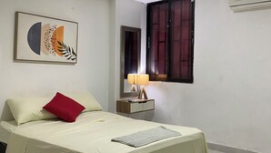 Un dormitorio con cama, mesita de noche, lámpara, espejo y aire acondicionado.