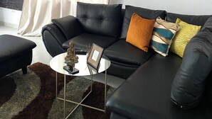 Una sala de estar con un sofá de cuero negro, un reloj redondo negro, una pequeña mesa de centro redonda y un cuadro enmarcado.