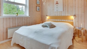 A bedroom with a wooden headboard, a bedside table with a book, a window with a view of trees, and a wall-mounted picture.