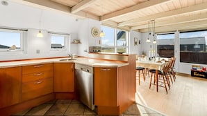 Una cucina moderna con mobili in legno, lavastoviglie e un'ampia isola. C'è un'area pranzo con sedie e tavolo in legno.