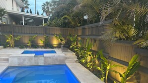 Ein Swimmingpool mit zwei Bereichen, umgeben von einem Holenzaun und verschiedenen tropischen Pflanzen.
