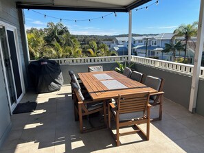 Un patio cubierto con una mesa y sillas de madera, una parrilla y vistas a casas y árboles.