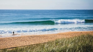 Ein Strand mit Wellen und einer Person, die mit einem Surfbrett entlanggeht.