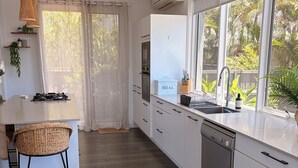 Eine moderne Küche mit weißen Schränken, einem Einbauofen, einem Geschirrspüler und einem großen Fenster mit Blick auf Grünflächen.