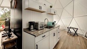 Una cocina compacta con armarios blancos, encimera de granito, cafetera, tostadora y un lavabo.