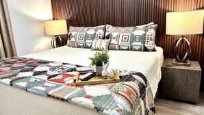 A neatly made bed with a quilt, a bedside table with a lamp, and a small potted plant.