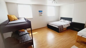 Une chambre avec un lit superposé, un lit simple et un bureau. Deux fenêtres laissent entrer la lumière naturelle.