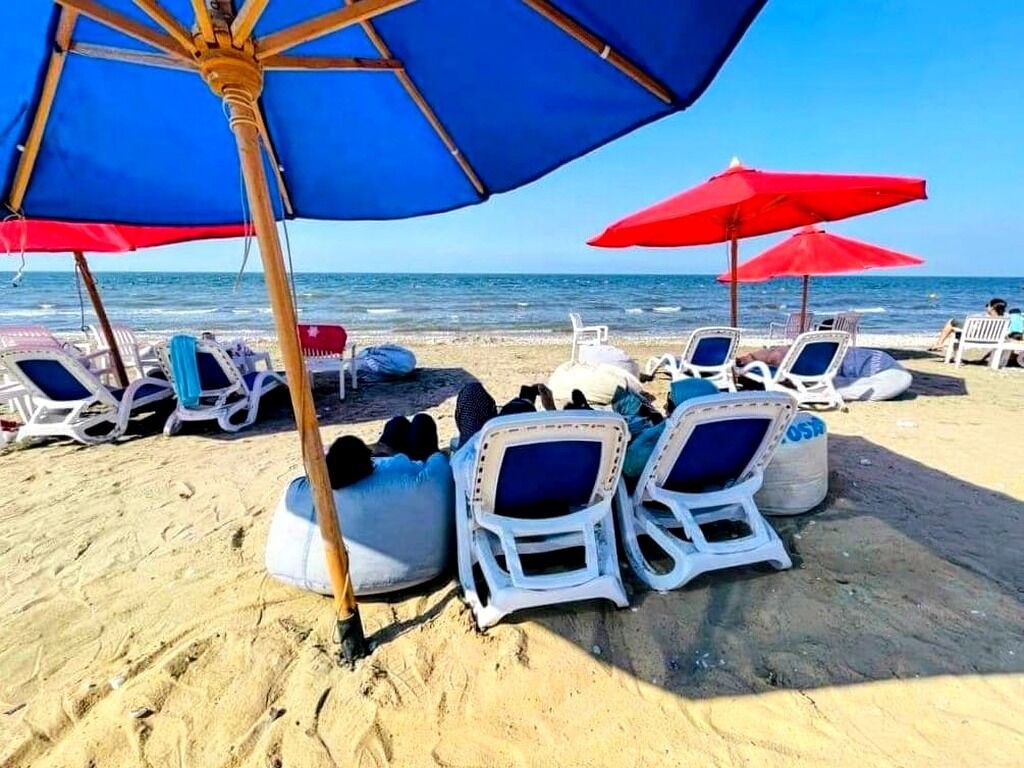 A beach with white lounge chairs and red umbrellas.