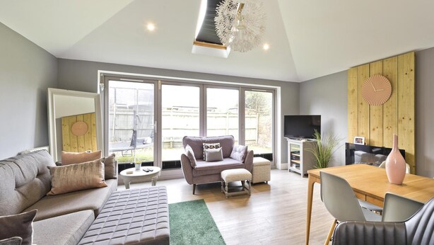 A spacious living room with a grey sofa, a smaller grey armchair, a wooden dining table, and a TV stand. - Twickenham Green (Twickenham)