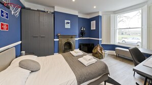 A hotel room with a bed, a desk, a chair, a fireplace, and a window with a view of the outside. - Twickenham Green (Twickenham)