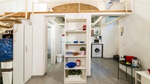 A compact kitchen with a built-in washing machine, a small dining area, and a loft space above. - Vico Santo Spirito di Palazzo 34 (Naples)