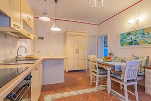 A kitchen with a dining area, white cabinets, a tiled backsplash, and a painting on the wall.