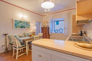 A kitchen with a central island, a dining area with a table and chairs, a wooden cabinet, and a window with a view. - Apartament Vista capomare (Capoliveri)