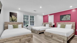 Habitación de hotel con tres camas de madera, ropa de cama blanca, una pared de acento rosa y una ventana con persianas.