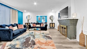Una sala moderna con una pared azul de acento, una chimenea y un televisor grande.