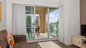 A modern apartment with a balcony, a sofa, a TV stand, and a dining area. - Belle Escapes - Glenelg Seaside Apartment (Glenelg)