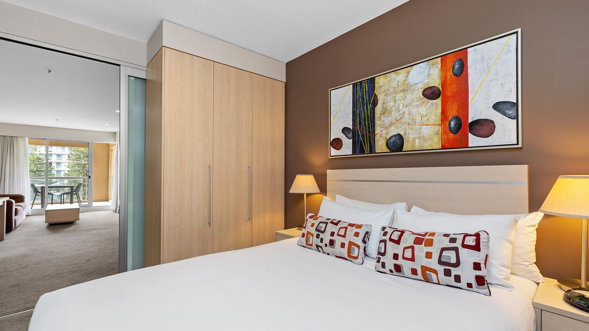 Ein Hotelzimmer mit einem großen Bett, einem Holzschrank, einem Bild an der Wand und einem Balkon mit Blick.