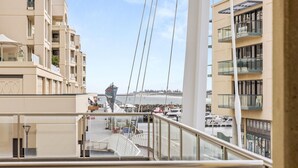 Udsigt over kysten fra en balkon med udsigt over en havn med både, en moler og en fjern kystlinje.