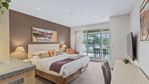 A modern hotel room with a bed, bedside lamps, a desk, a television, and a balcony with a view.