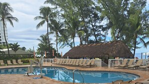 A pool area with lounge chairs, a thatched-roof structure, and palm trees. - Beautiful 1 bedroom condo on the beach in Pompano Beach (Pompano Beach)