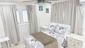 A bedroom with a bed, nightstands, a ceiling fan, and a window with curtains. - Beachfront Villa on Andros Island, Bahamas (Andros Town)