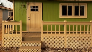 A small, single-story house with a green exterior and white trim. It features a front door with a small window above it, a front porch with a white railing, and a small deck area. - Beachfront Villa on Andros Island, Bahamas (Andros Town)