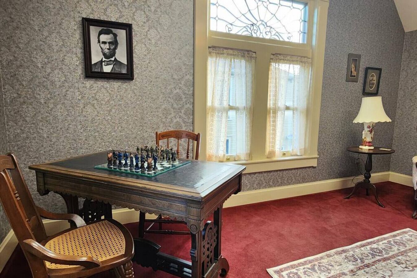 Ein Zimmer mit Schachbrett auf einem Holztisch, einem gerahmten Bild an der Wand und einem Fenster mit Vorhängen.