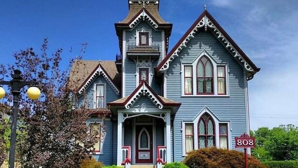 A Victorian-style house with a prominent front porch, a central entrance, and a large front yard.
